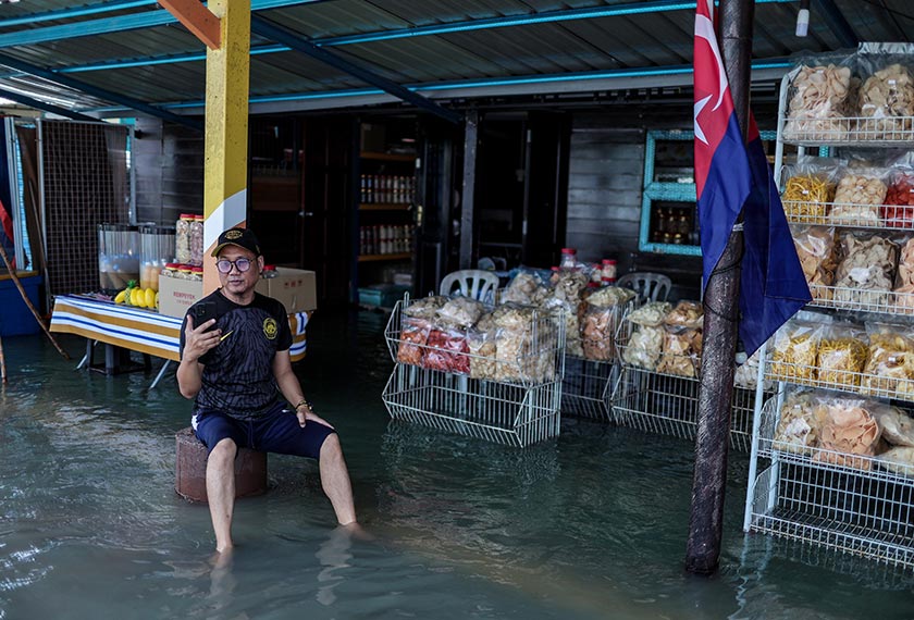 Peniaga, Zulkifli Mohd Hafan, duduk di hadapan gerainya yang dinaiki air susulan fenomena air pasang besar di Kukup hari ini. - Foto Bernama